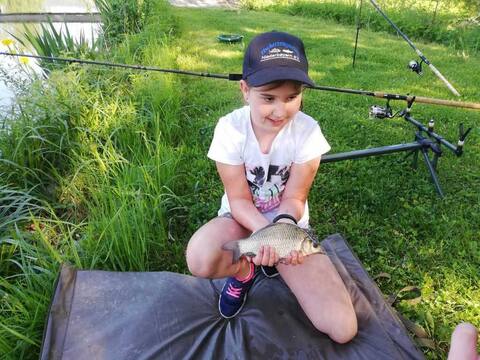 Kind mit Kappe sitzt mit seinem Fisch auf der Abhakmatte
