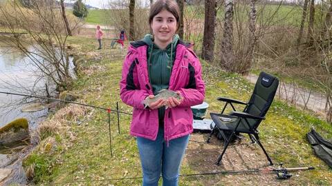 Jungfischerin in pinker Jacke zeigt einen Fisch am Furthweiher