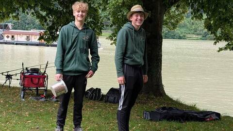 Zwei Jugendliche in Vereinsshirts unter einem Baum am Ufer